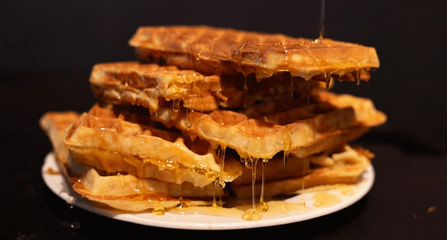Stack of golden Belgian waffles with honey being poured over them